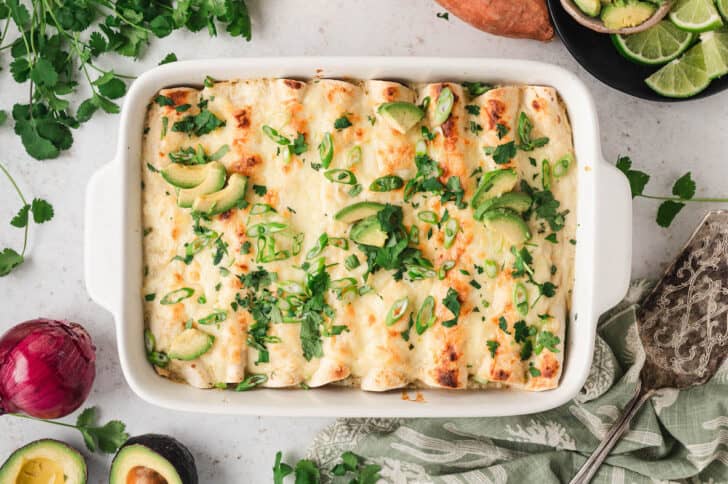 A white baking dish filled with a veggie enchilada recipe topped with green herbs and avocado.