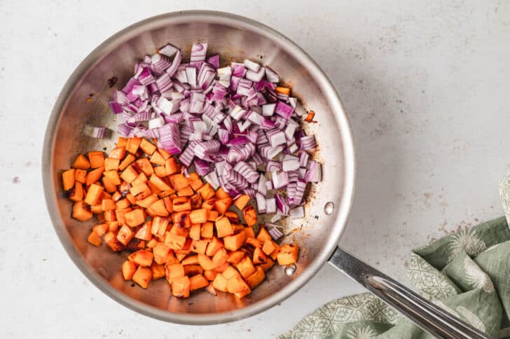 A stainless steel skillet filled with chopped sweet potato and red onion.