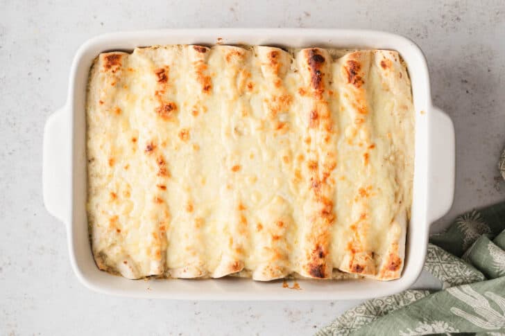 A rectangle white baking dish filled with veggie enchiladas topped with cheese.