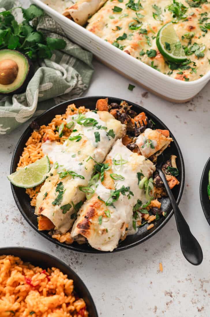 A black plate filled with orange rice and a veggie enchiladas recipe.