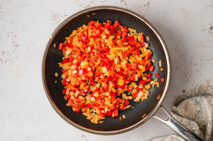 Sauteed red bell pepper and onion in a black skillet.