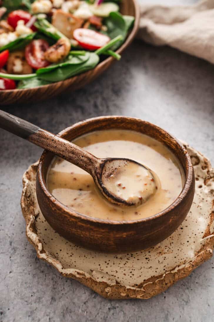 A wooden bowl filled with honey mustard dressing, with a wooden spoon lifting some out.