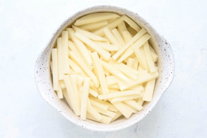 Sliced potatoes soaking in water in a rustic bowl.