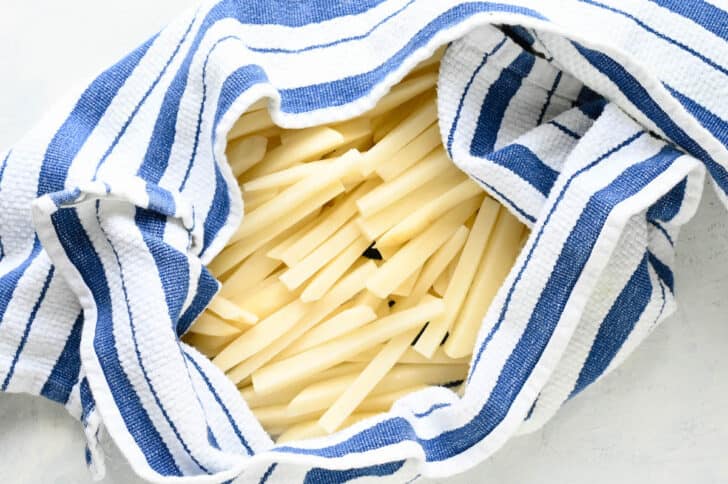 Sliced potatoes wrapped in a blue and white striped towel.