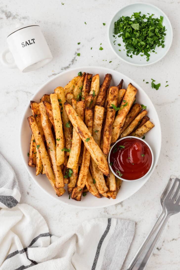 Oven baked French fries on a parchment-lined tray with a ramekin of ketchup.