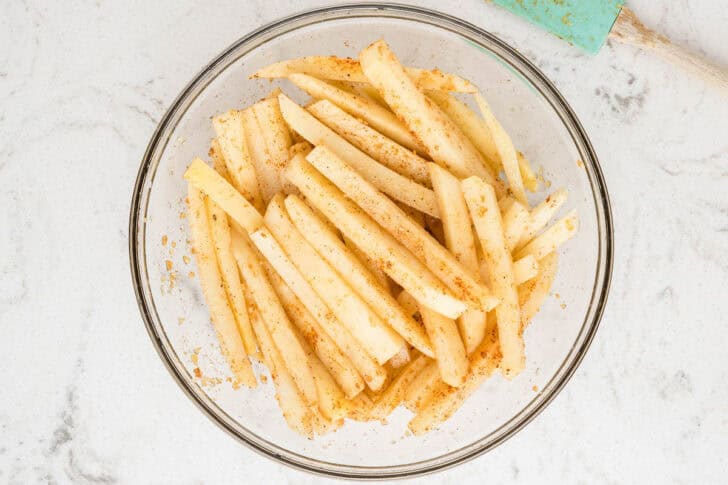 Sliced potatoes tossed with seasonings in a glass bowl.