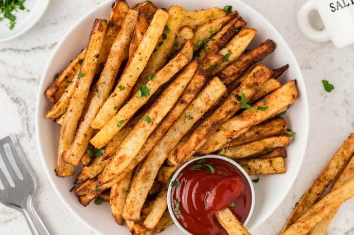 Oven French fries on a parchment-lined tray with a ramekin of ketchup.