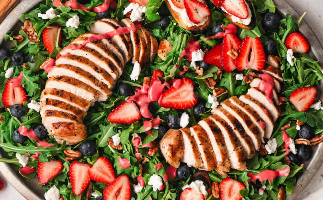 A large oval platter filled with summer salad made with berries, arugula and grilled chicken.