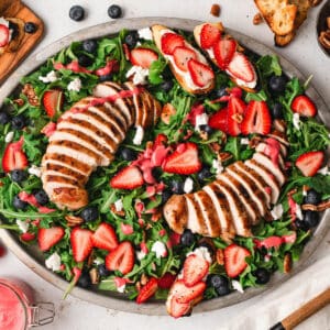 A large oval platter filled with summer salad made with berries, arugula and grilled chicken.