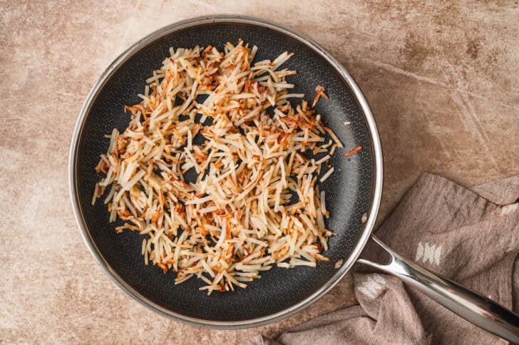 Shredded hash browns cooking in a nonstick skillet.