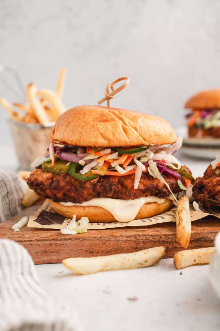 The best fried chicken sandwich recipe plated on a piece of newspaper on a wooden board, with fries.