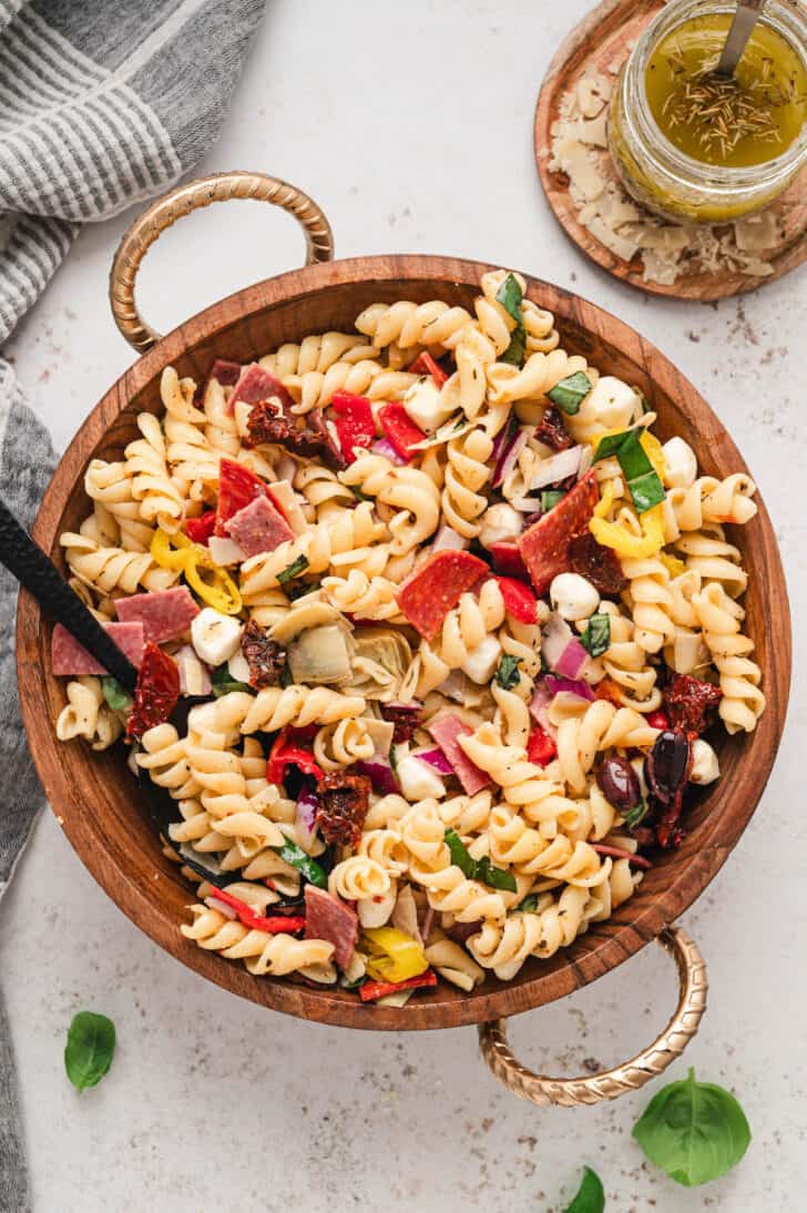 A wooden bowl filled with pasta salad with Italian dressing and antipasto ingredients.