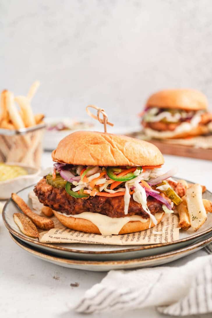A fried chicken sandwich recipe plated on a piece of newspaper on a plate, with fries.