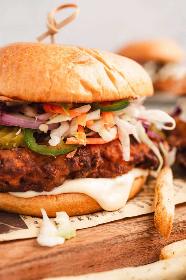The best fried chicken sandwich topped with coleslaw, on a wooden cutting board.