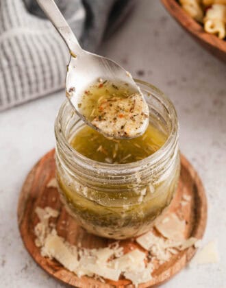 A spoon lifting homemade Italian dressing out of a glass jar.