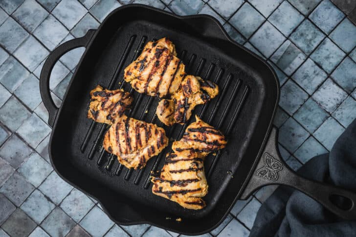 Poultry thighs being grilled on a cast iron grill pan.