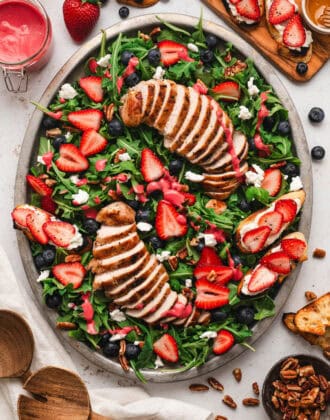 A large oval platter filled with summer salad made with berries, arugula and grilled chicken.