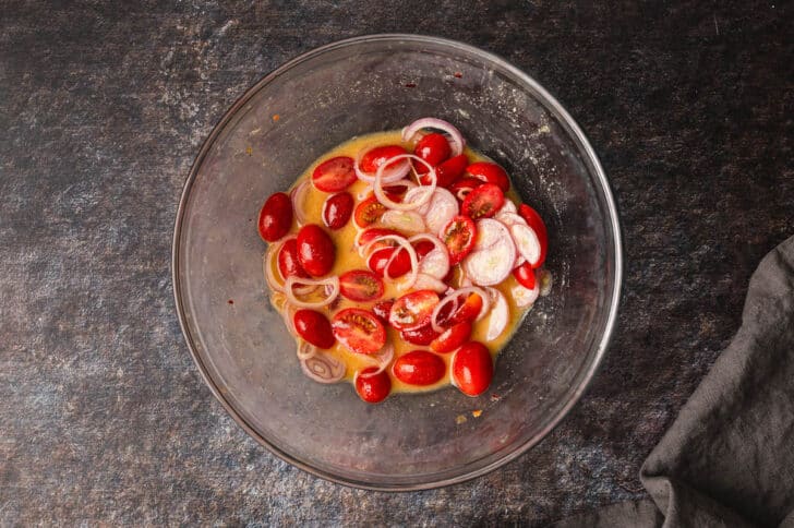 A glass bowl filled with salad dressing, grape tomatoes and sliced shallots.