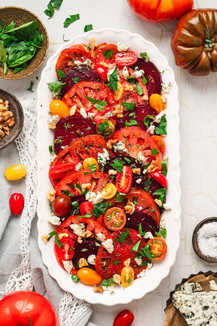 A white oval platter filled with beet salad with tomatoes.