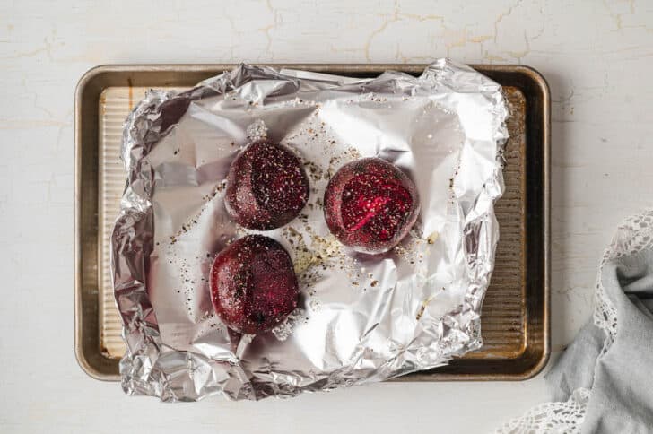 Red root vegetables on a piece of foil on a baking pan.