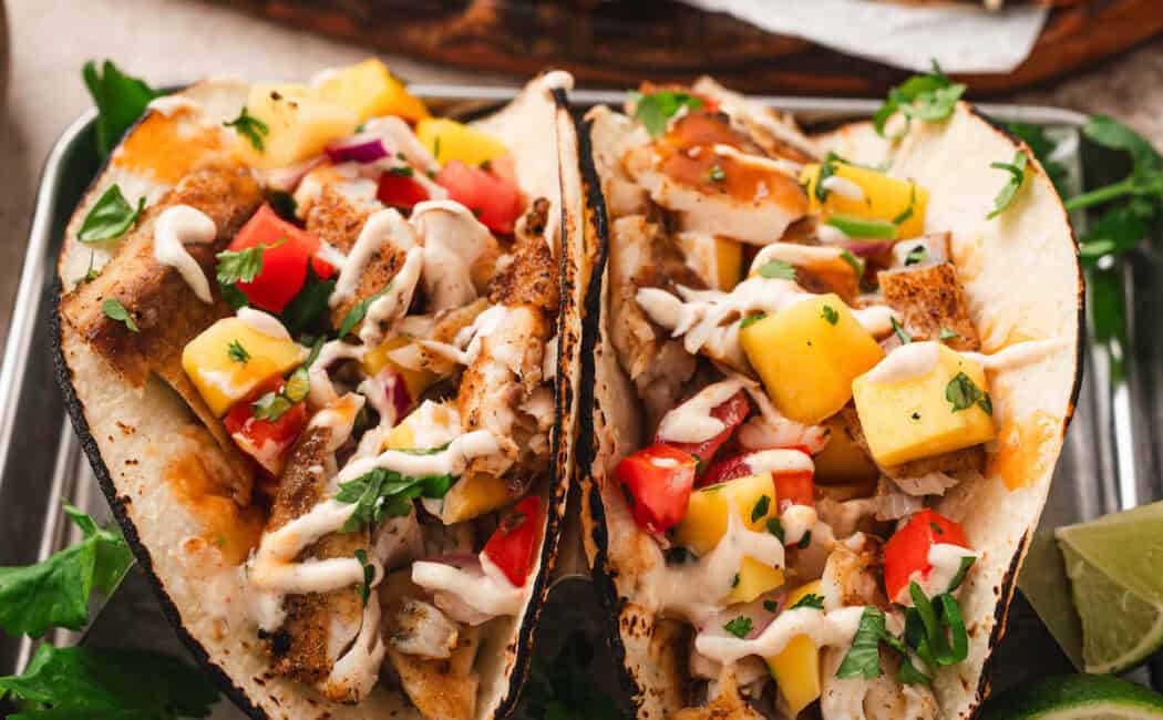 A fish taco topped with tropical fruit salsa and drizzled with creamy sauce.