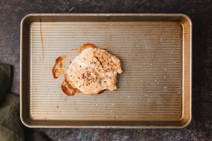 A rimmed baking pan with one cooked chicken breast on it.