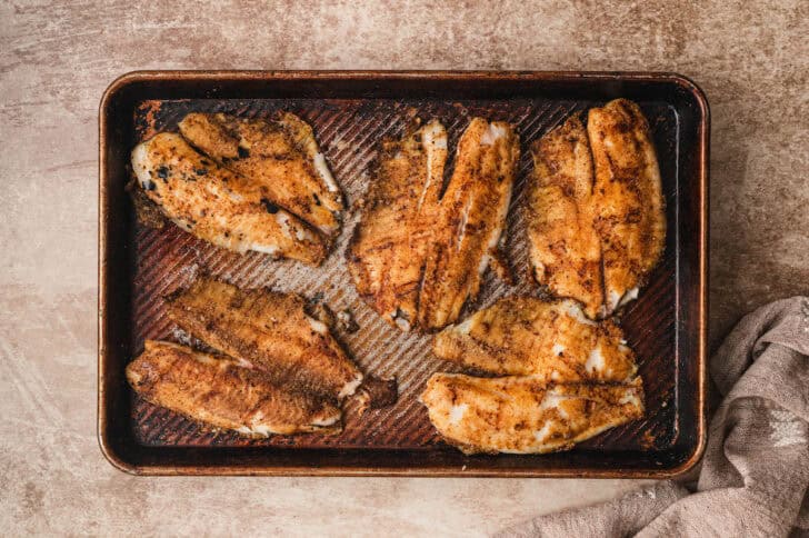 A rimmed baking pan topped with grilled fillets of tilapia.