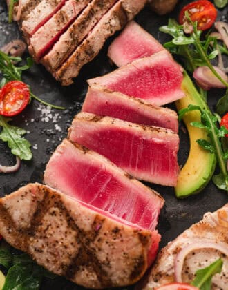 A sliced grilled tuna steak surrounded by salad ingredients.