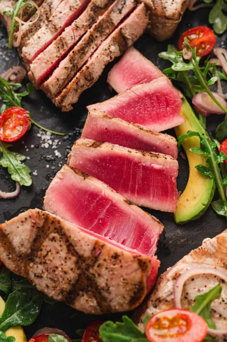 A sliced grilled tuna steak surrounded by salad ingredients.