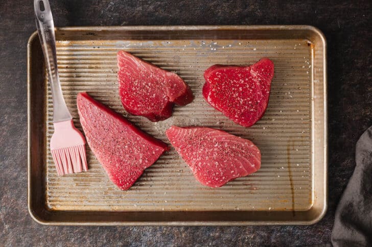 A rimmed baking pan with four pieces of raw fish.