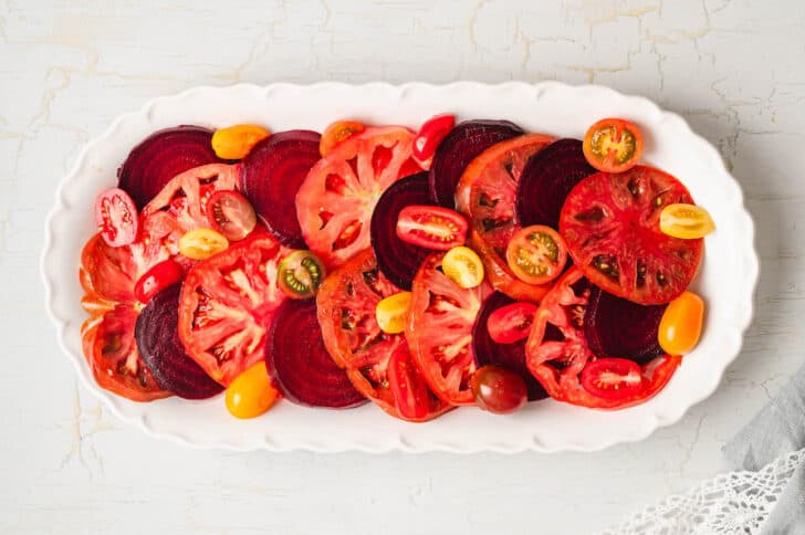 A white platter with sliced tomatoes and beets arranged on it.
