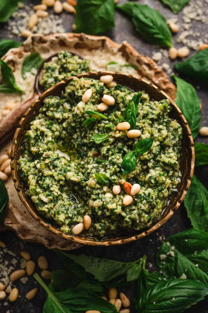 A bowl of homemade pesto sauce garnished with pine nuts and fresh basil.