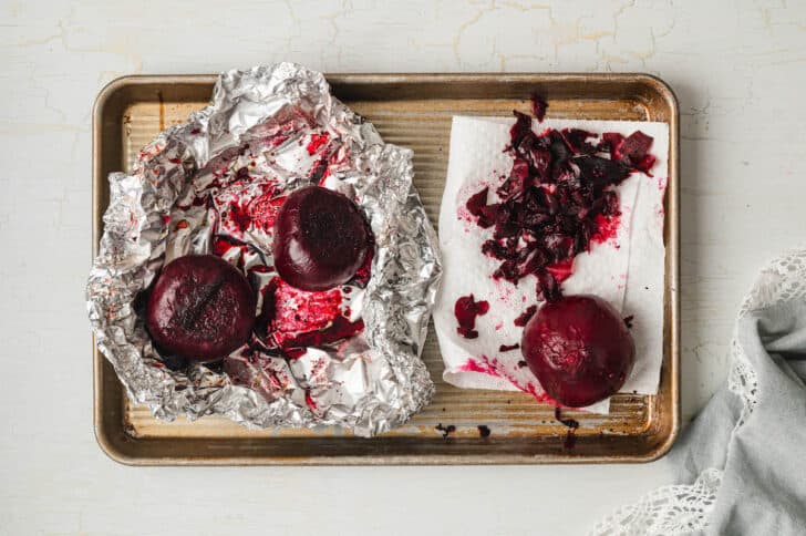 Roasted beets in the process of being peeled on a baking pan.