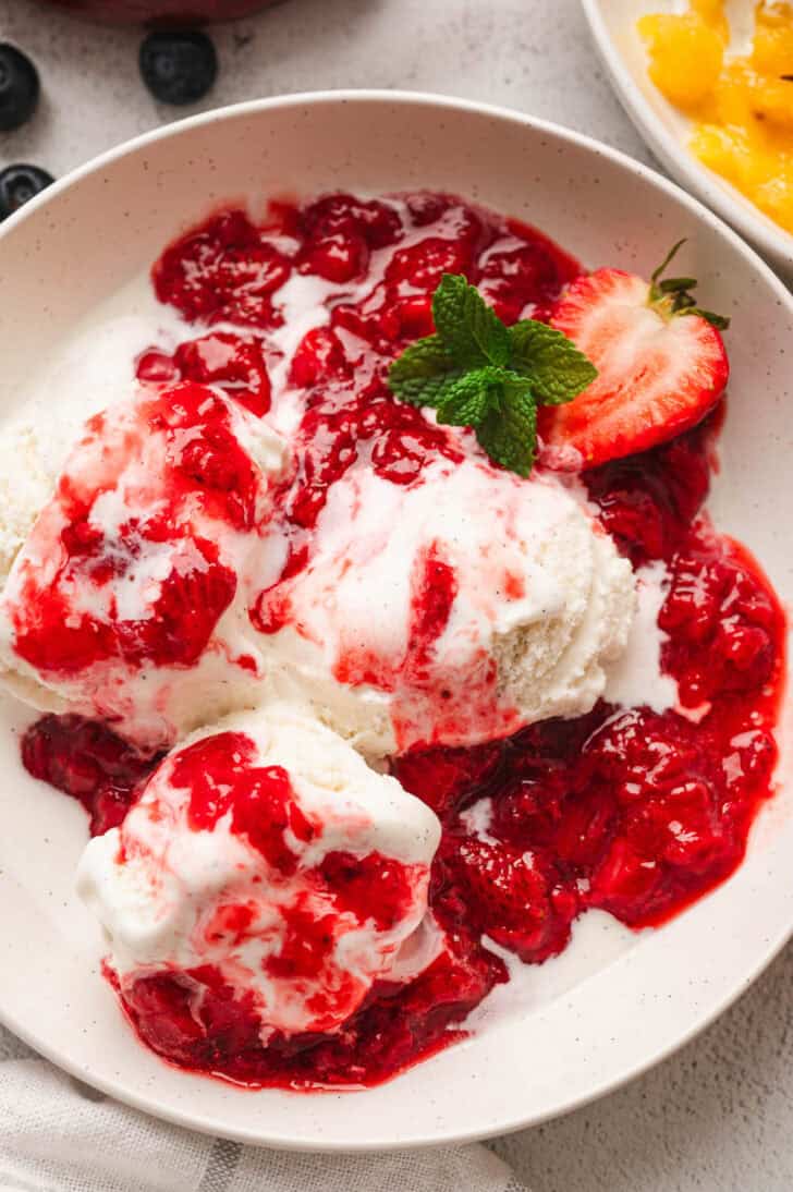 A bowl filled with vanilla ice cream topped with strawberry ice cream topping.