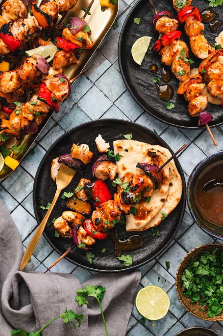 A meal scene with black plates filled with chicken kabobs on the grill and naan bread.