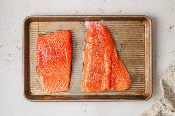 Two pieces of raw orange fish on a rimmed baking pan.