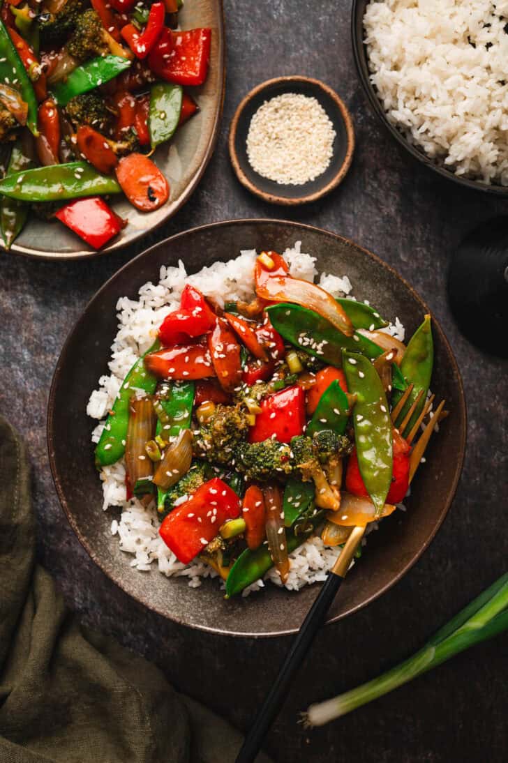 Stir fry vegetables served over rice in a dark bowl.