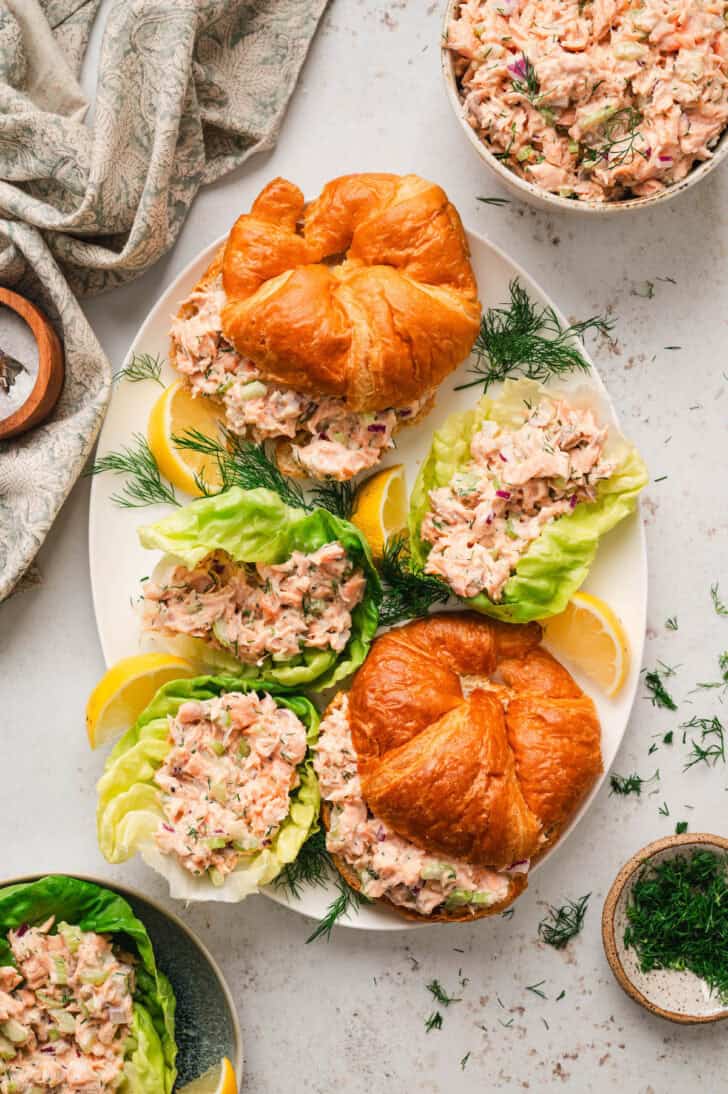 Salmon salad shown served on lettuce wraps and in croissants on a large white platter.