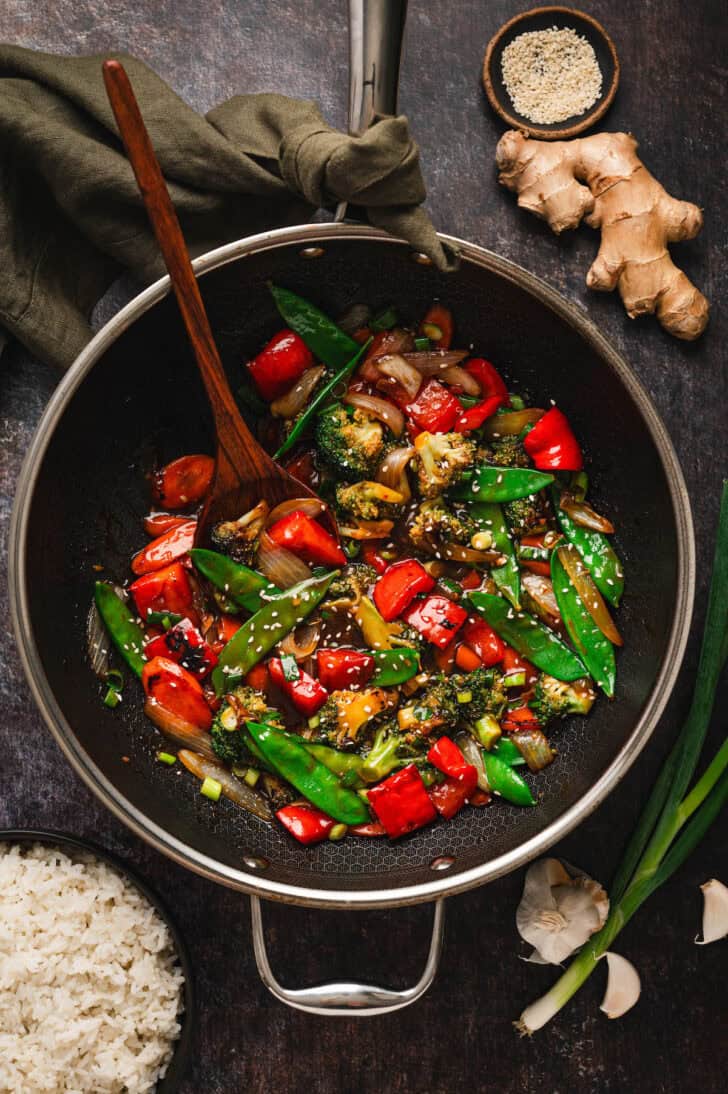 A black skillet filled with a veggie stir fry recipe, with a wooden spoon in it.