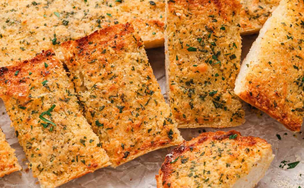 A loaf of homemade garlic bread on a wooden cutting board on a light surface.
