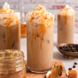 A tall glass of caramel iced coffee in front of a textured brick wall.