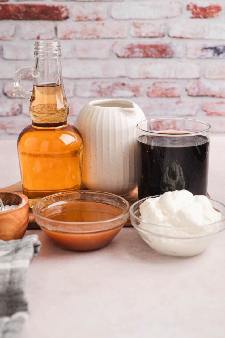 Ingredients for a coffeehouse drink in front of a texture brick wall, including whipped cream and dessert sauce.