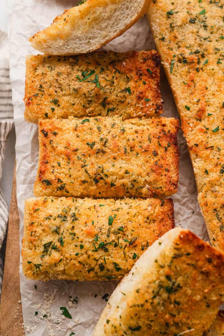 A loaf of the best garlic bread recipe on a wooden cutting board on a light surface.