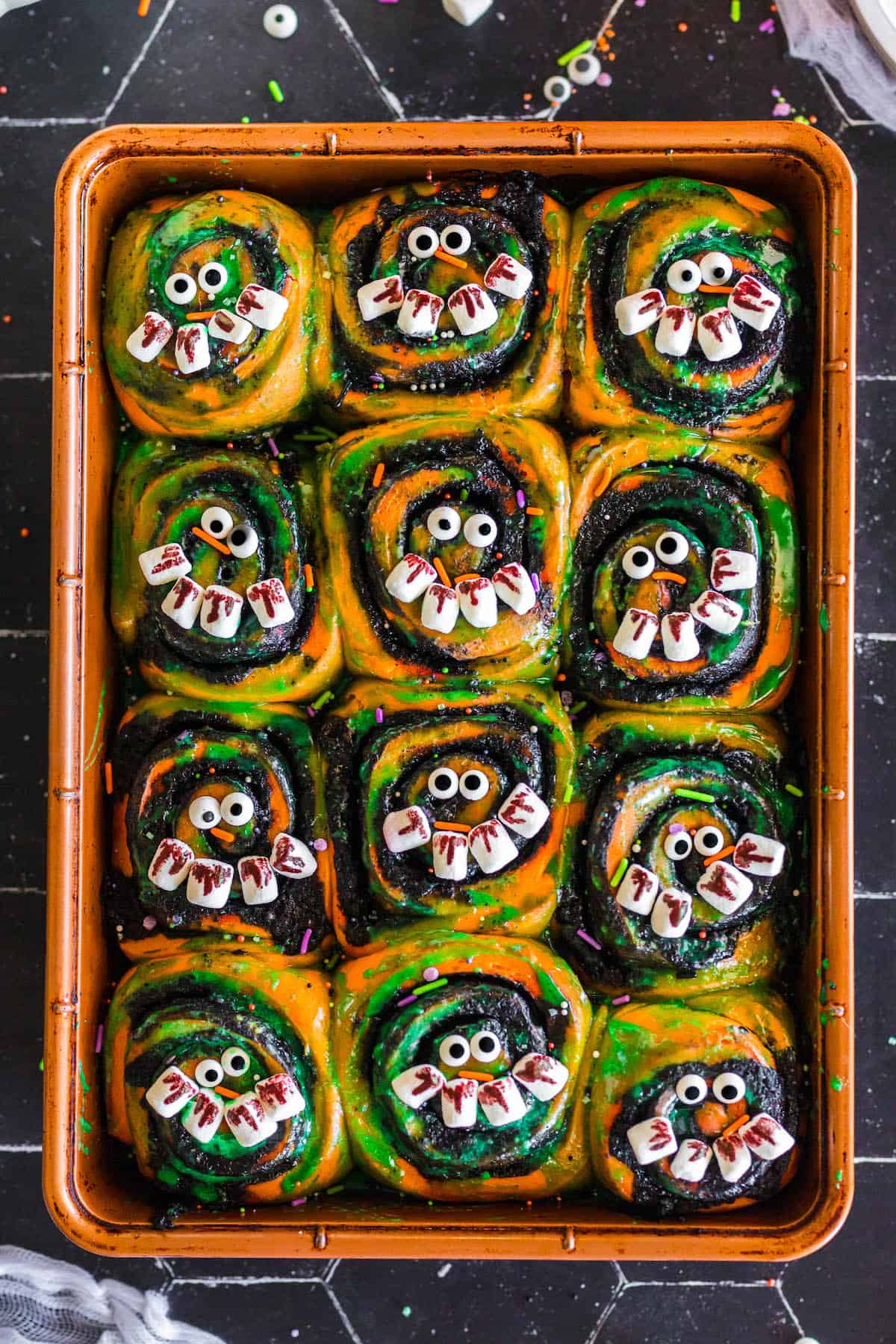 Halloween cinnamon rolls in an orange baking pan.