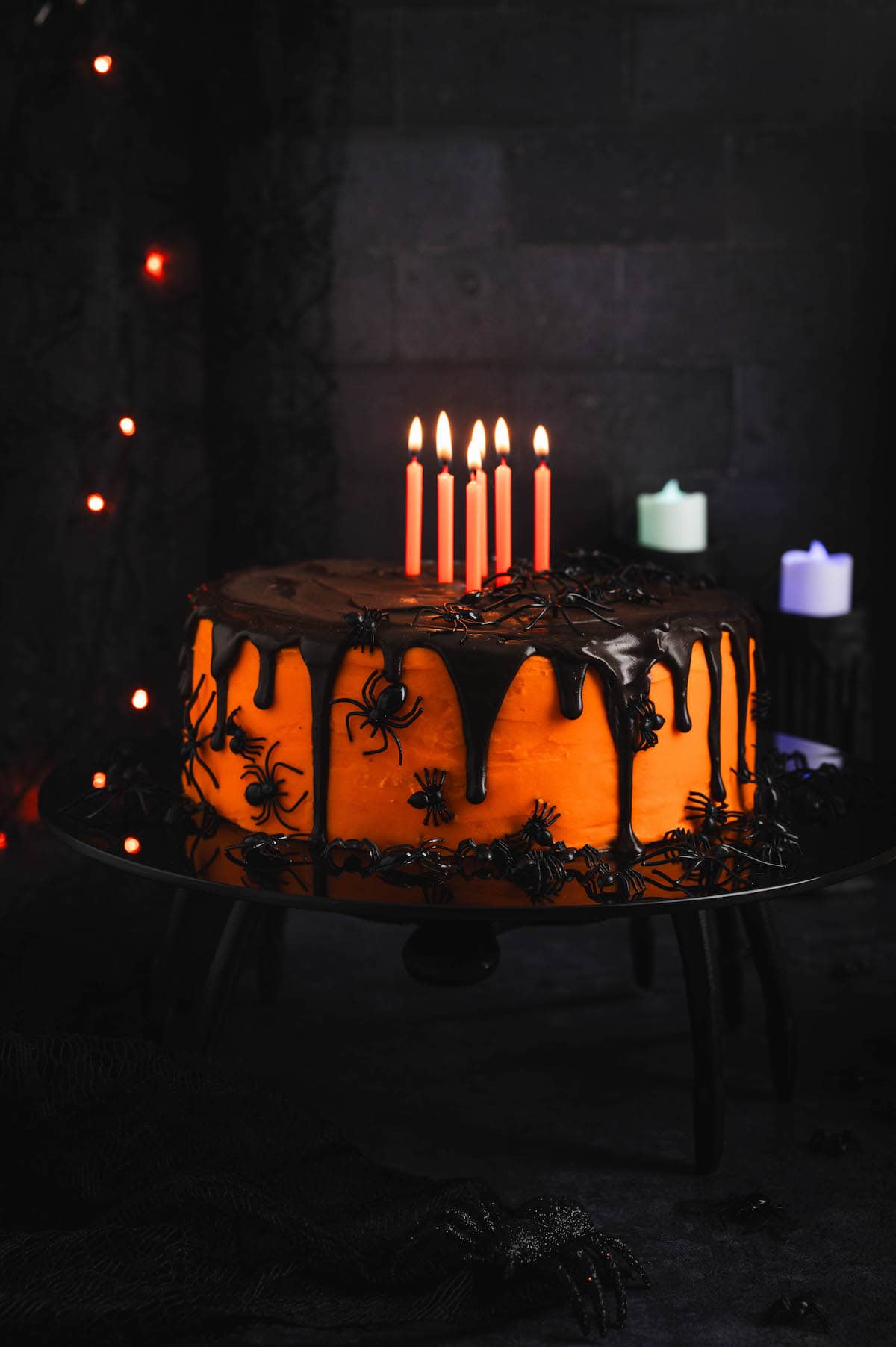 A Halloween birthday cake topped with orange candles in front of a dark backdrop.