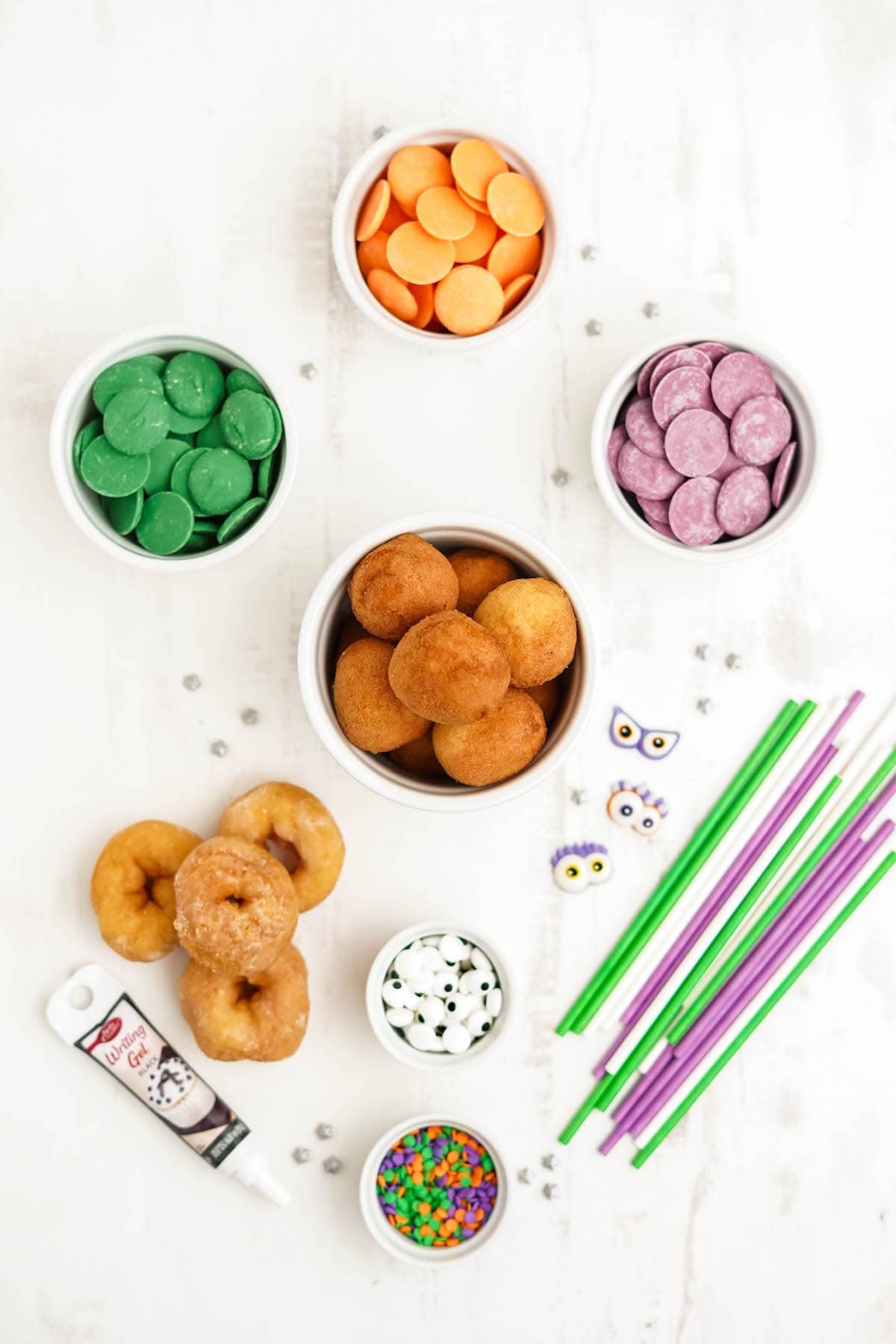 Ingredients on a white surface, including mini donuts and donut holes, candy melts and sprinkles.