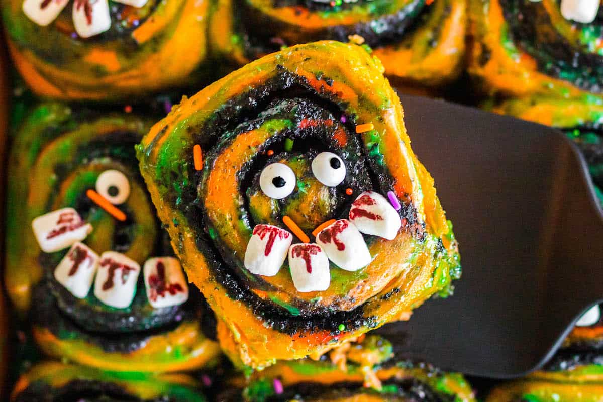 A Halloween breakfast for kids that is a cinnamon roll being lifted out of a pan.