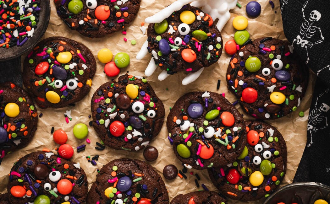 A spread of Halloween cookies with a skeleton hand lifting up one cookie.