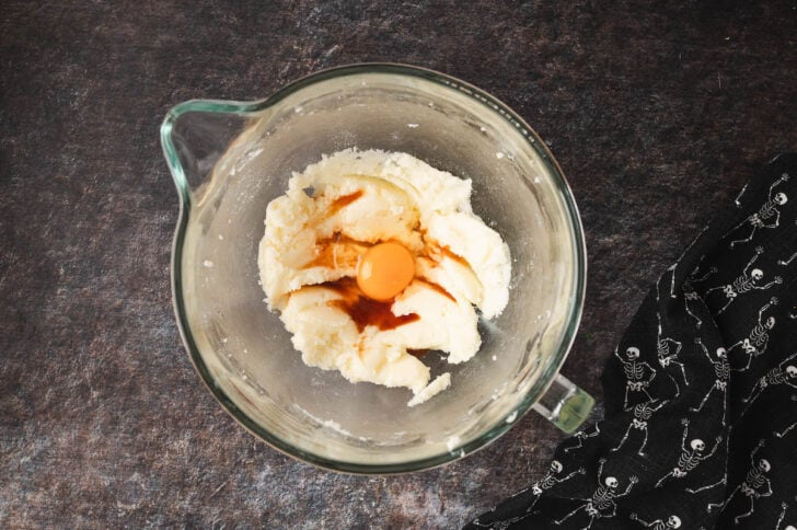 A glass bowl of a stand mixer filled with creamed butter and sugar, and egg and vanilla extract.