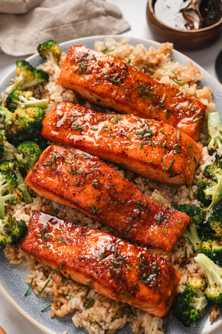 Four pieces of honey glazed salmon on a platter, served over rice and broccoli.